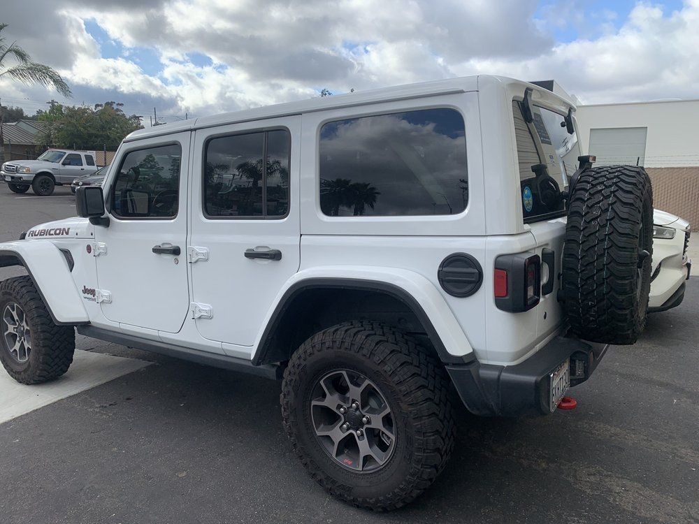 A white jeep wrangler is parked next to a white car in a parking lot.