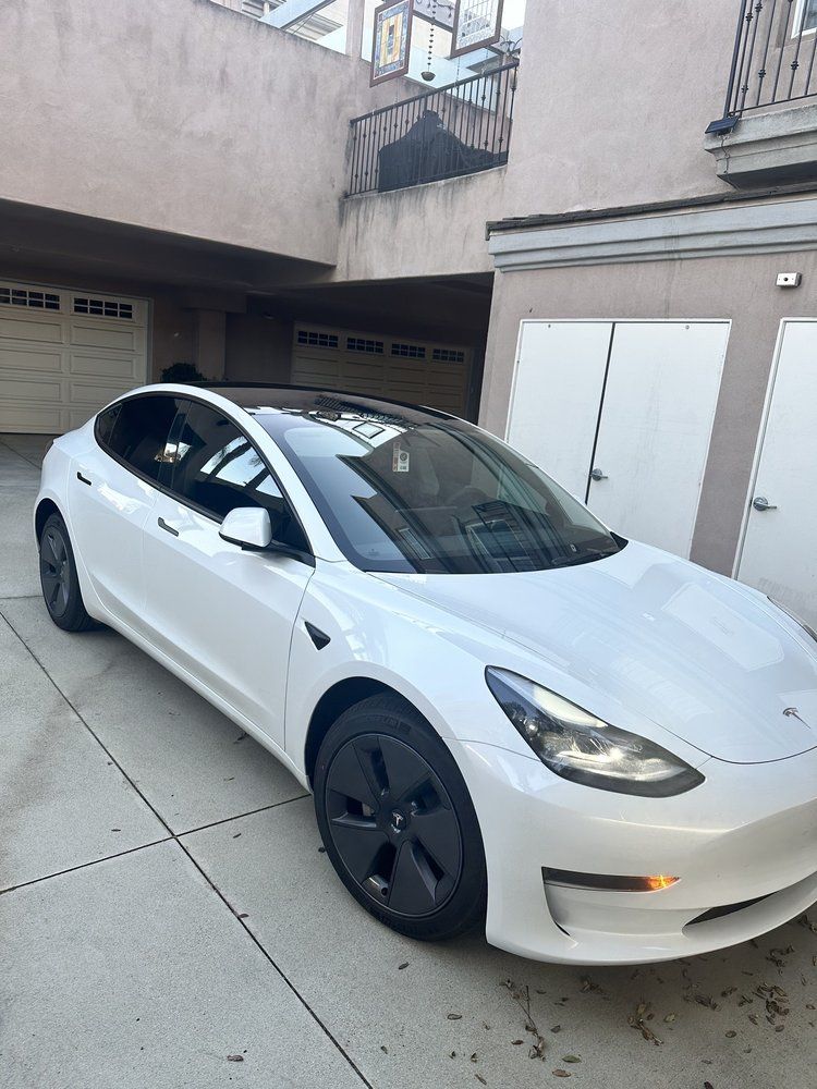 A white tesla model 3 is parked in a driveway in front of a building.