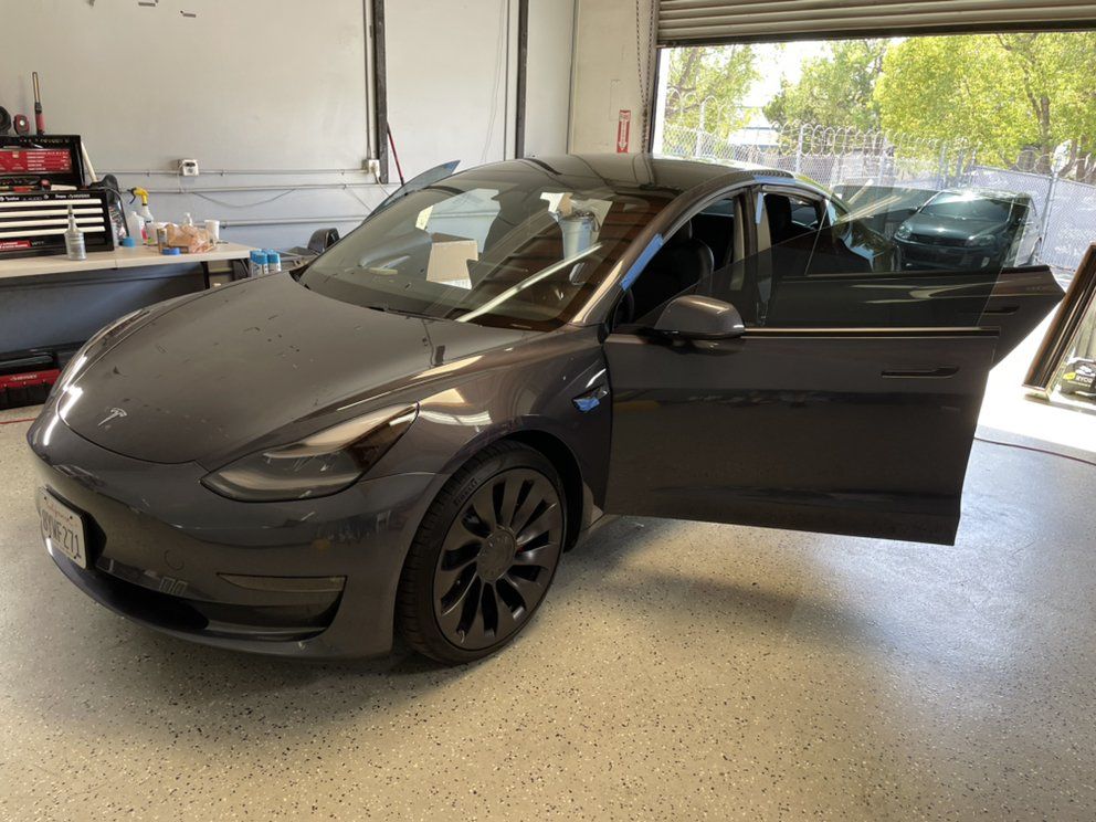 A tesla model 3 is parked in a garage with its doors open.