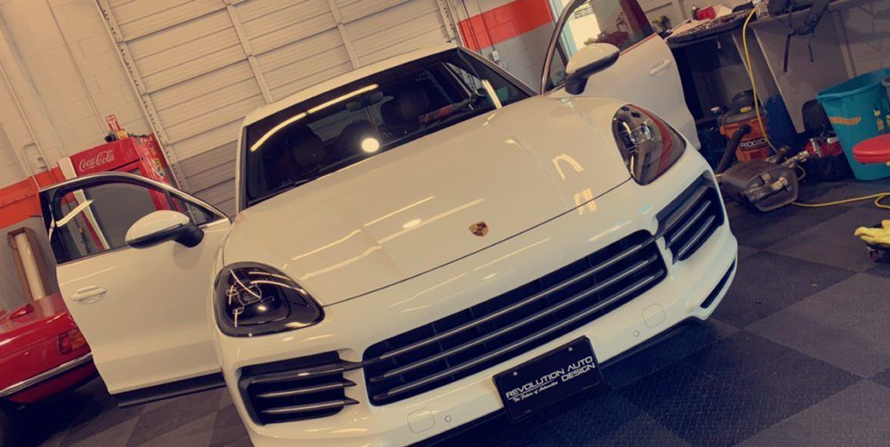 A white porsche cayenne is parked in a garage with its doors open.