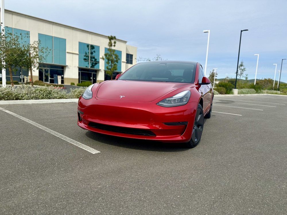 A red tesla model 3 is parked in a parking lot in front of a building.
