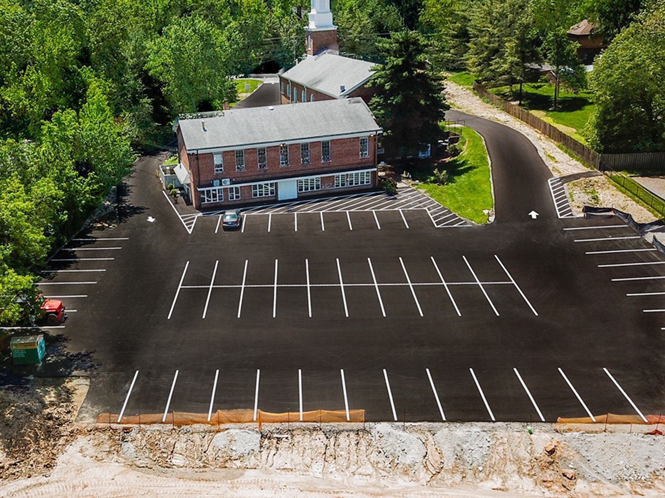 Aerial view of a brick building beside an empty parking lot surrounded by trees.