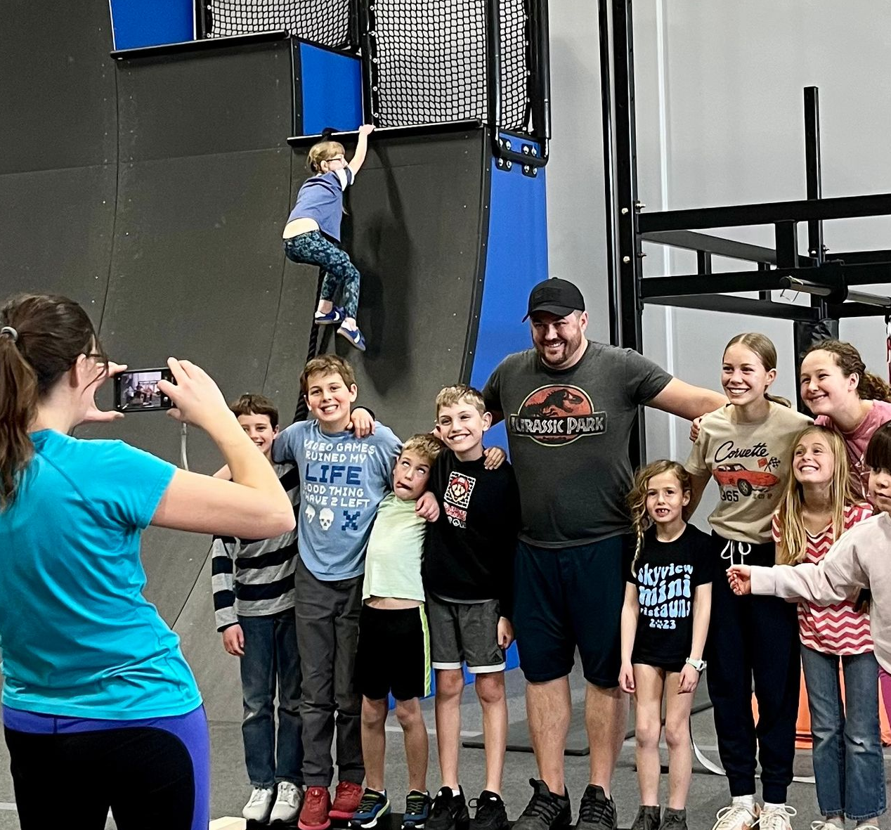Indoor obstacle course with blue and orange structures, gray mats, and a metal overhead rig.