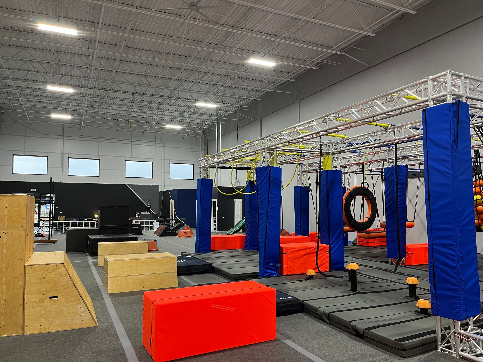 Indoor obstacle course with climbing frames, padded pillars, and platforms.