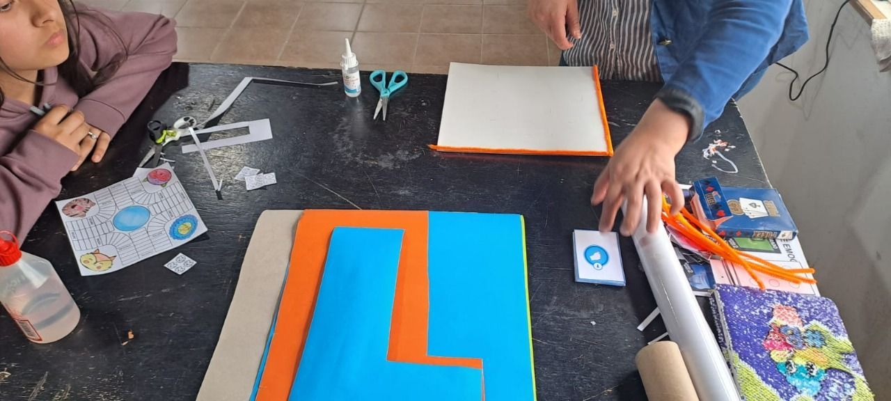 Personas haciendo manualidades con papel y materiales de colores sobre una mesa negra.