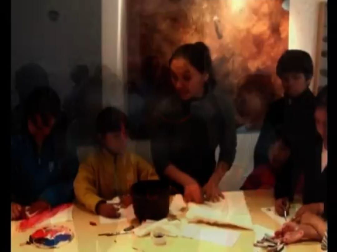 Una mujer y varios niños en una mesa, probablemente realizando un proyecto de arte.