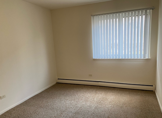 An empty bedroom with a window and blinds.