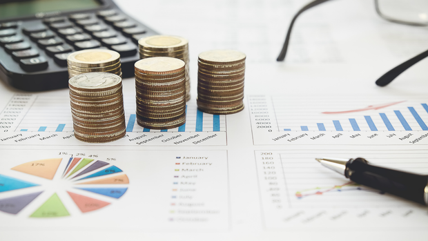 Stacks of coins, calculator, glasses, and pen on financial charts.