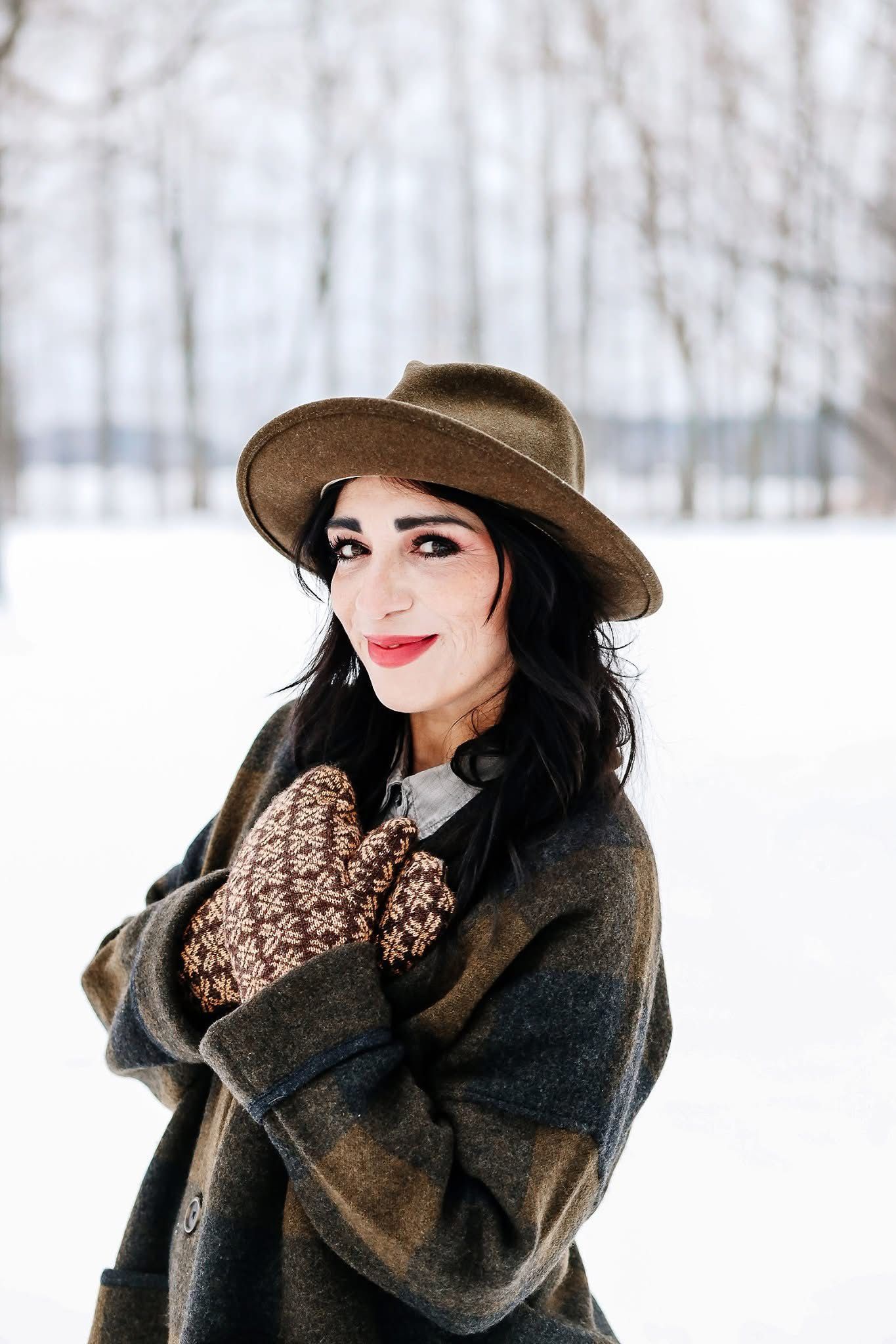 A woman wearing a hat and mittens is standing in the snow.