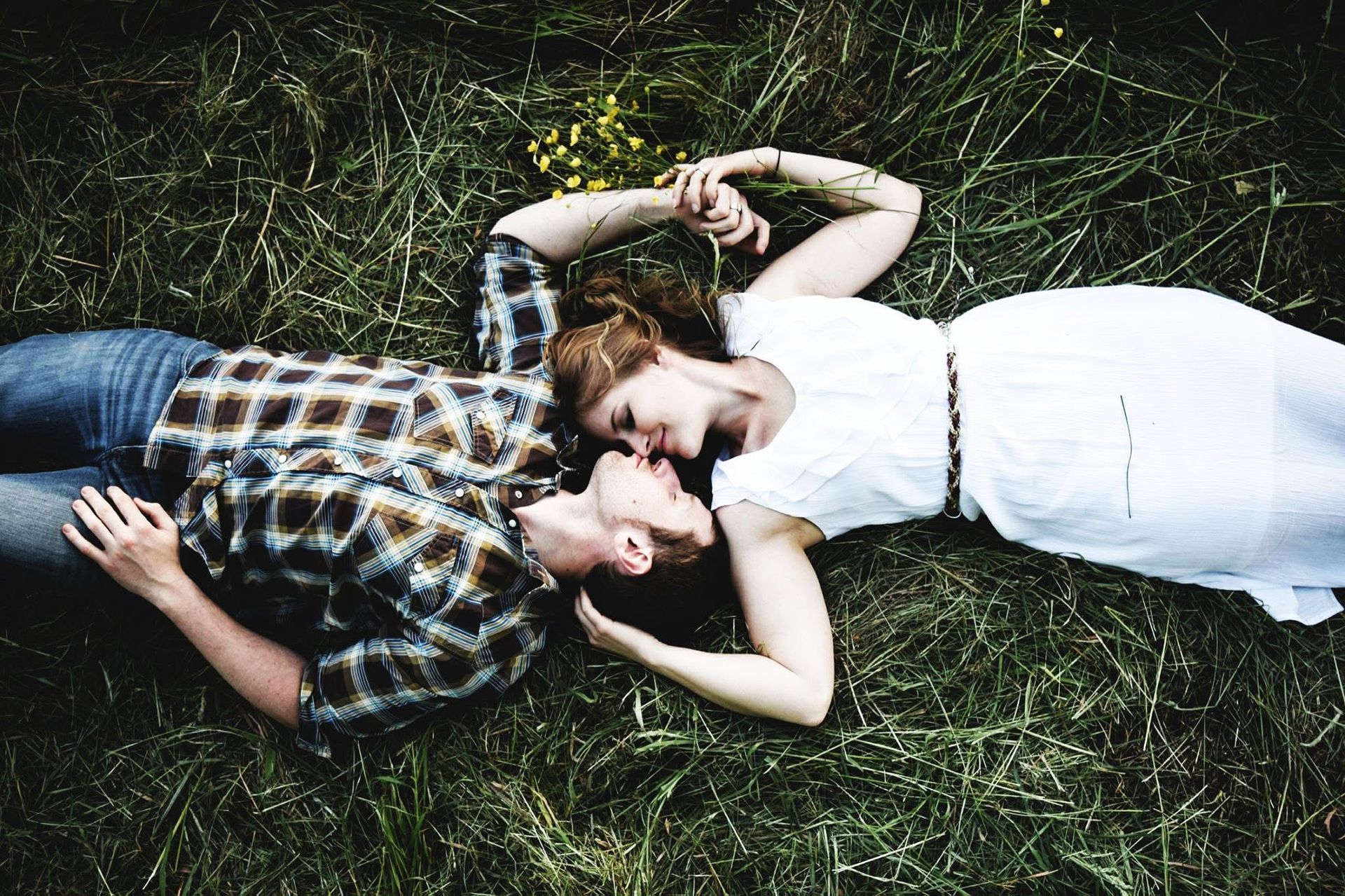 A man and a woman are laying on top of each other in the grass.