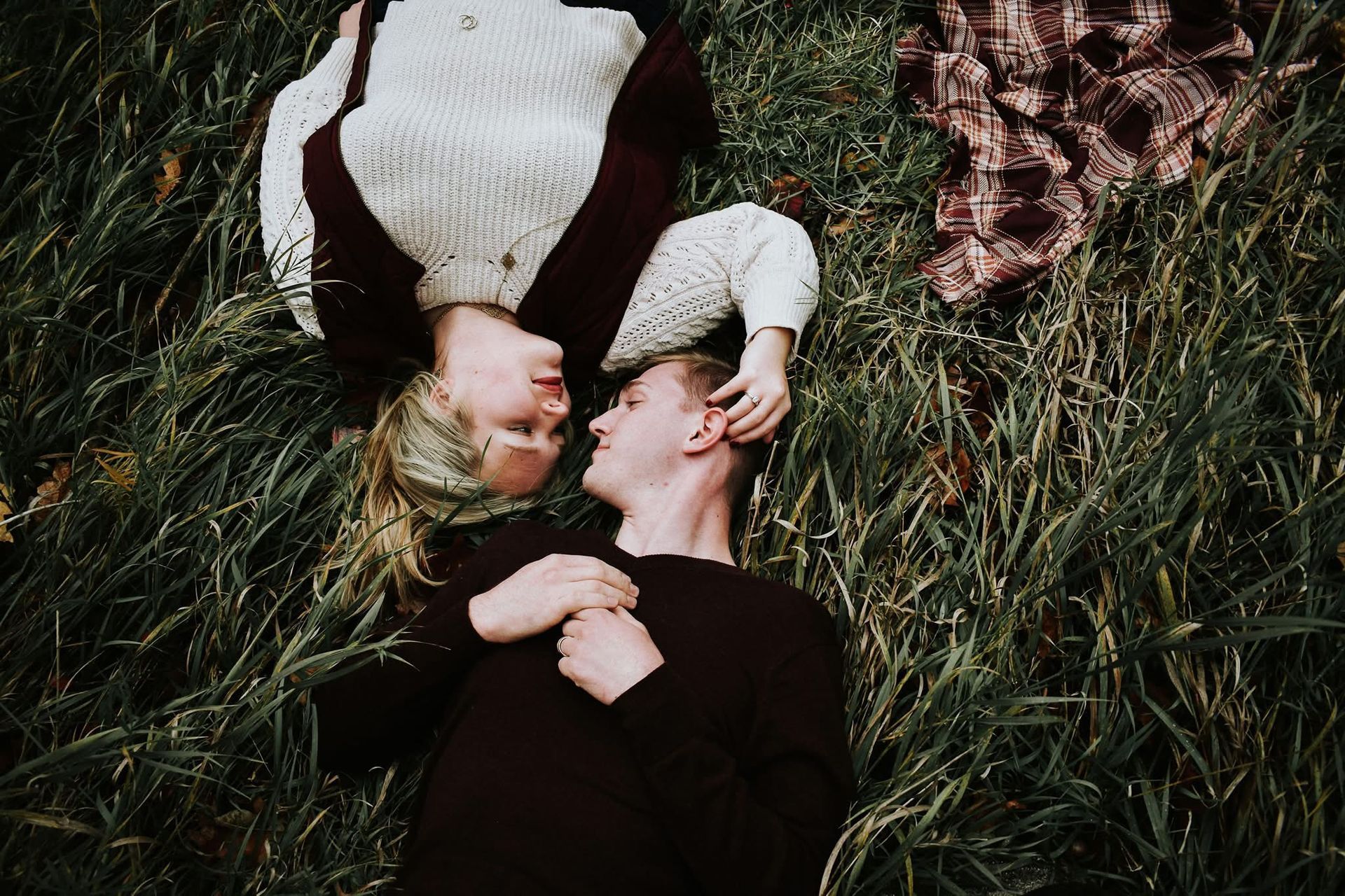 A man and a woman are laying in the grass looking at each other.
