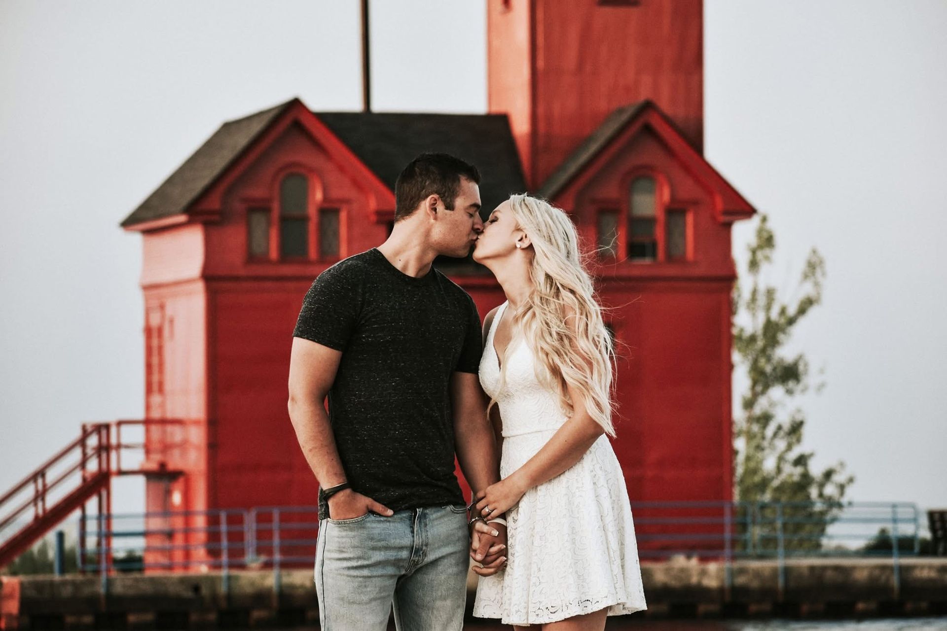 A man and a woman are kissing in front of a red building.