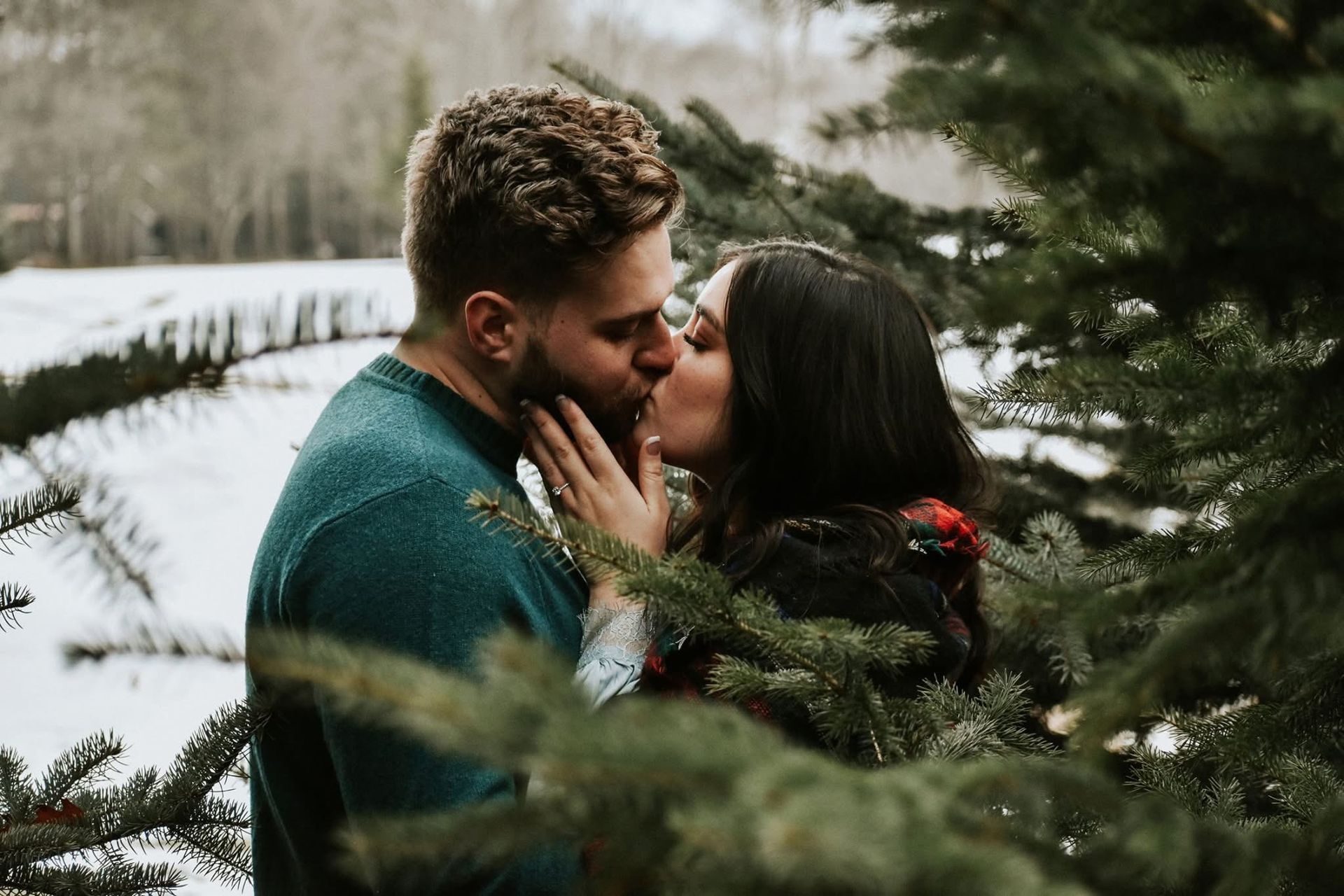 A man and a woman are kissing in front of a christmas tree.
