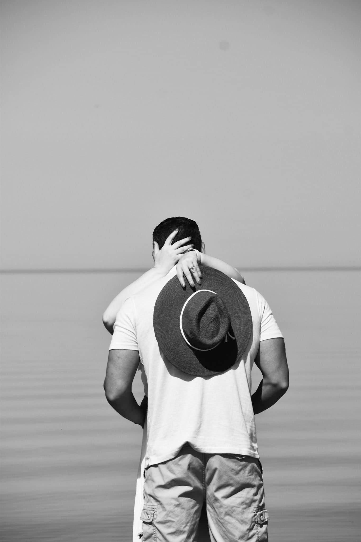 A woman is hugging a man while holding a hat on his back.