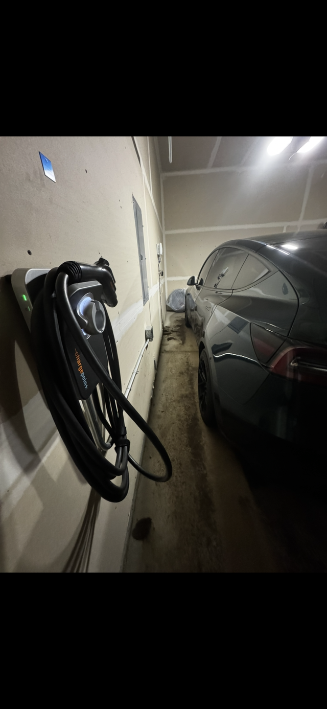 Electric vehicle charging station beside a parked black car in a garage with concrete walls.