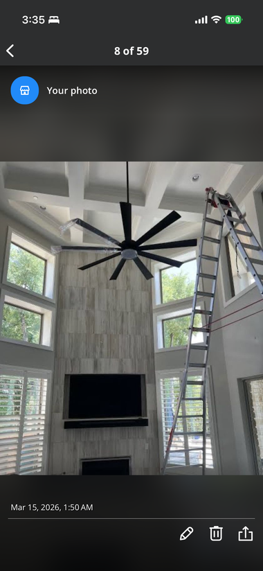 Tall living room with vaulted windows, a black ceiling fan, fireplace, and a ladder beside built-in shelves