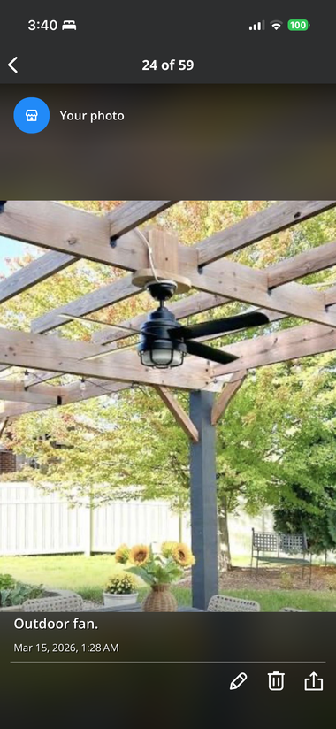 Black ceiling fan under a wooden pergola in a garden patio with greenery around it