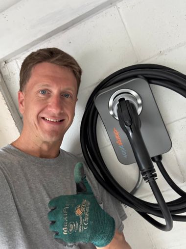 Smiling person giving thumbs up beside a wall-mounted EV charger with coiled cable