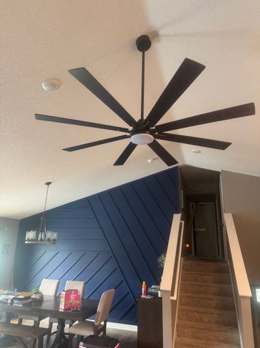 Living room with a large ceiling fan, blue accent wall, dining table, and staircase