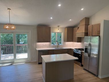 Modern kitchen with island, stainless steel refrigerator, wood cabinets, and sliding glass doors to a deck