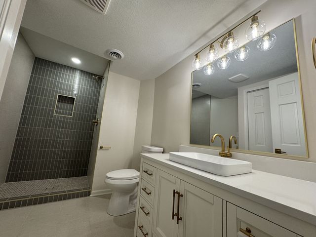 Modern bathroom with double vanity, large mirror, glass shower, and toilet.