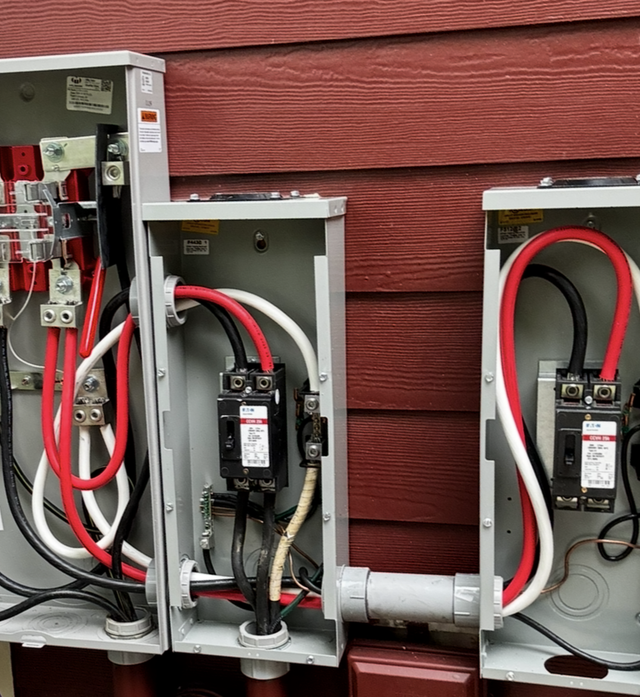 Three open electrical meter boxes with red and black wiring mounted on a red house exterior.
