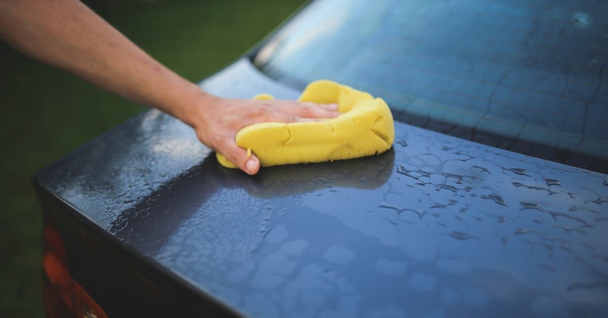 A person is cleaning a car with a yellow sponge.