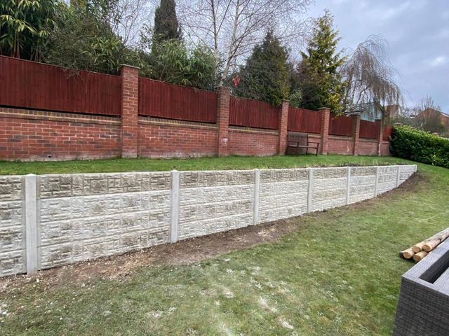 Stacked rock-faced concrete gravel boards forming a low retaining wall along a sloping lawn in Ilkeston