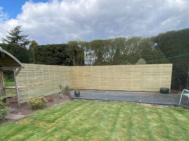 The slatted privacy screen seen across the lawn of a Keyworth garden with hedging behind