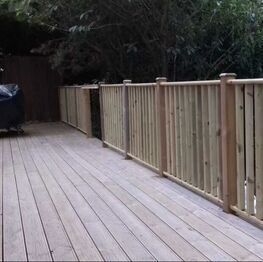 A raised timber deck with a matching balustrade running along the edge of a garden
