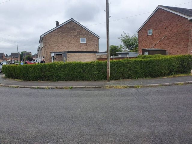 A large overgrown hedge running along a corner front boundary of a house in Selston before removal
