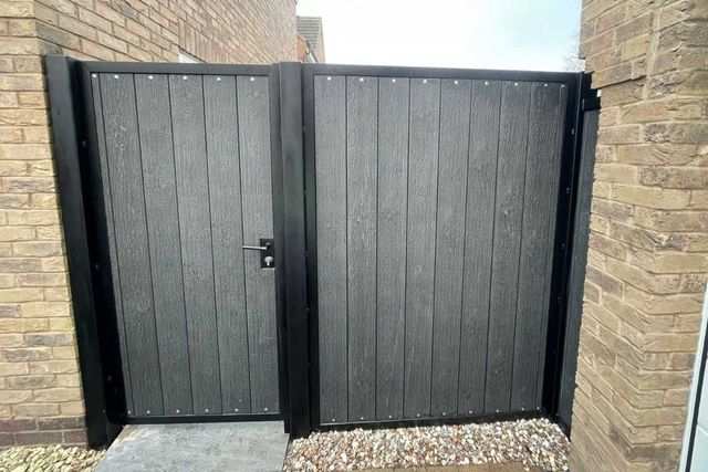 Black composite double gates in a metal frame between a house and garage in West Bridgford