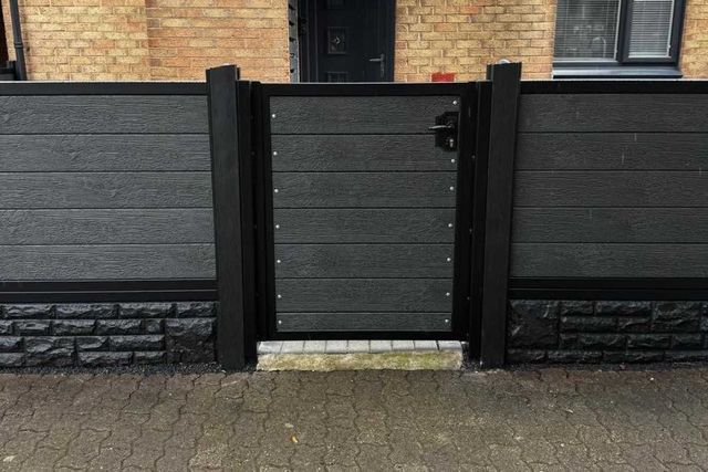 A black composite gate set between composite fence panels with a rock-effect base in Hucknall
