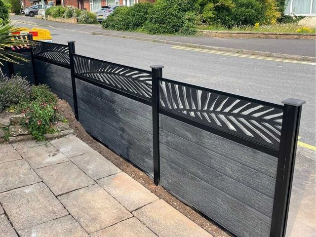 Anthracite embossed composite fencing with a palm leaf design screen topper beside a road