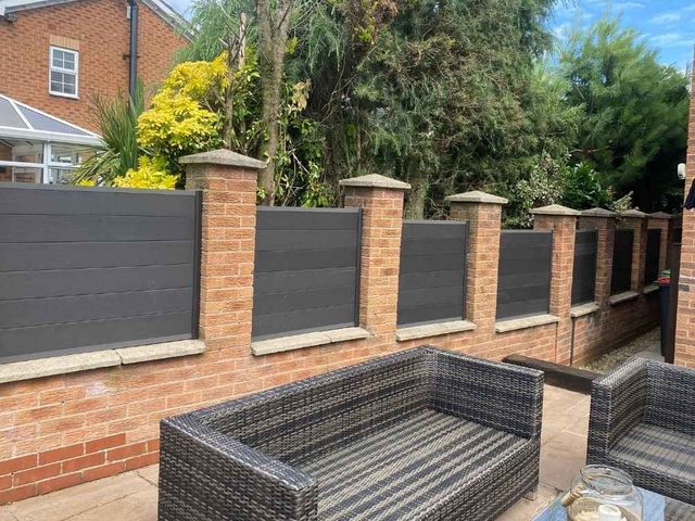 Anthracite grey composite panels fitted between brick pillars above a garden wall with a patio below