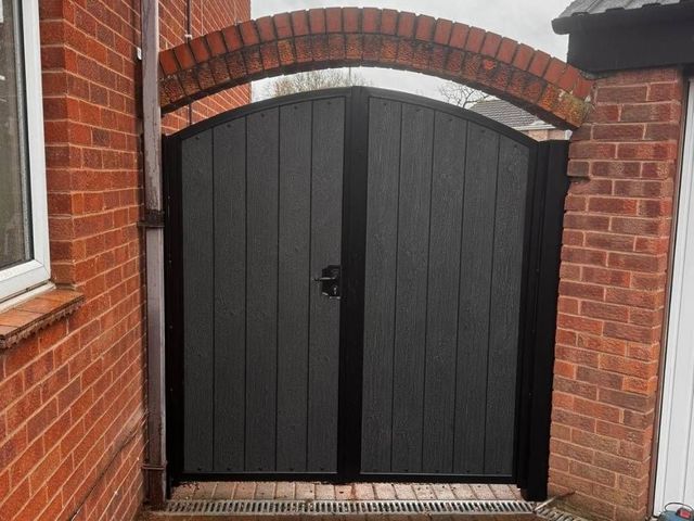 Black arched composite double gates fitted beneath a red brick arch in Arnold