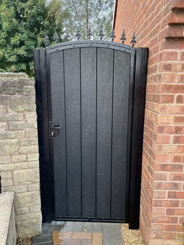 Black arched composite garden gate topped with cast fleur de lis finials