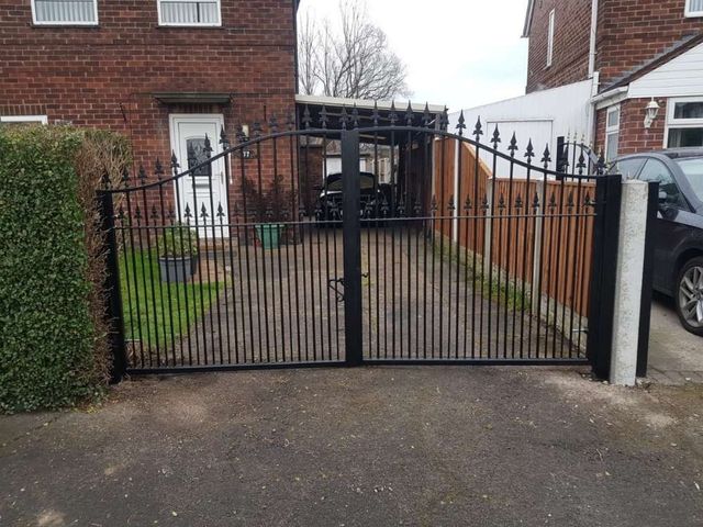 Black arched metal driveway gates with spear finials across a wide driveway