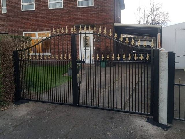 Black arched metal driveway gates with two rows of gold fleur de lis detailing