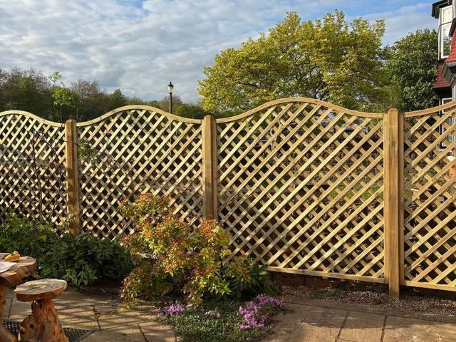 Tall arched top diamond trellis fence panels on timber posts above a paved patio garden