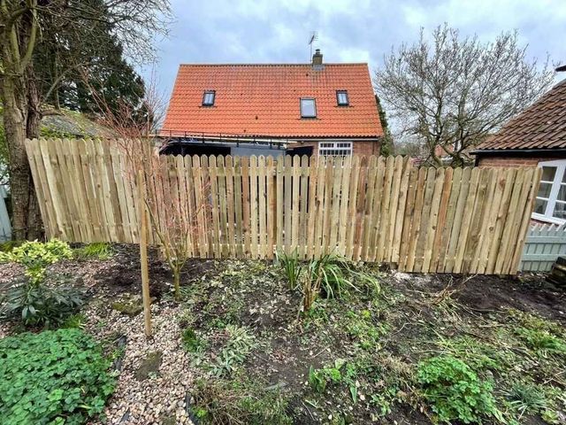 Full height round top picket fencing stepped down a slope across the rear of a garden in Nottingham