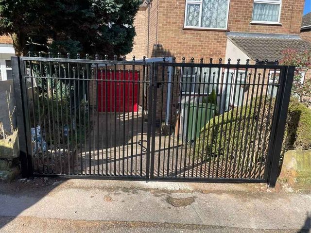Black metal driveway gates with ball tops between brick walls