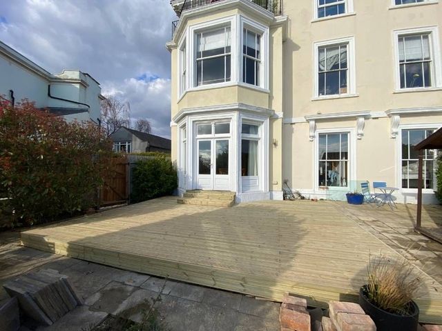 The finished timber deck laid across the full width of the rear elevation of a rendered Victorian house with a step up to the doors