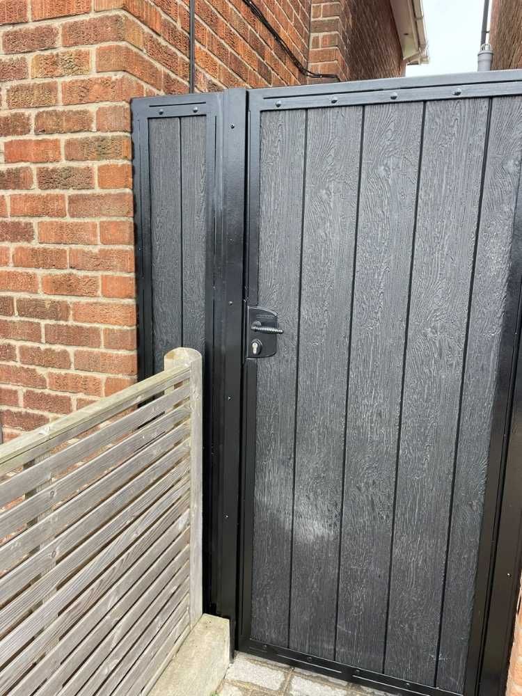 Black composite side gate with a narrow matching panel alongside it between two houses