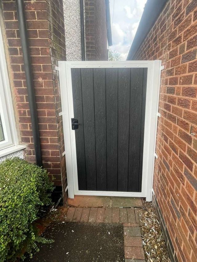 Black composite side gate in a white metal frame matching the house windows