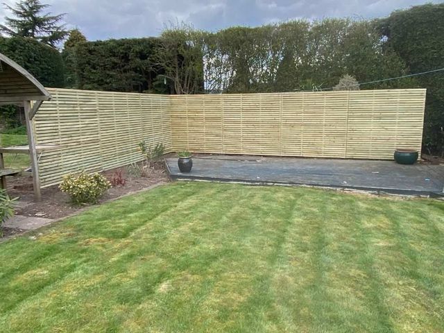 Slatted fencing used as a screen wrapping around a decking area with a mature hedge behind it