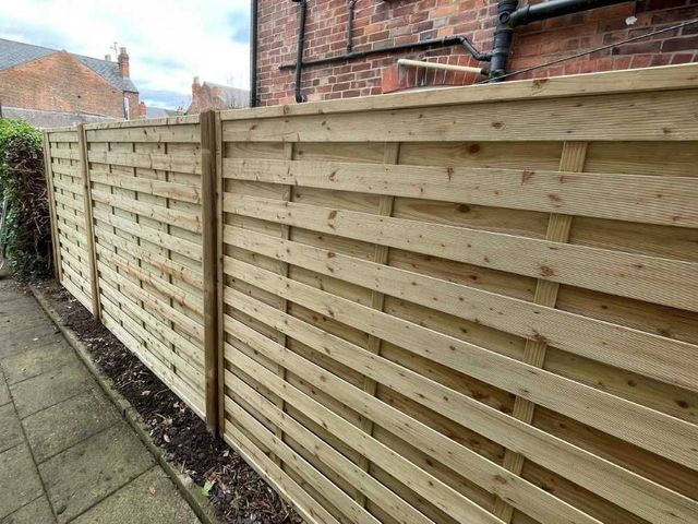 Close view of hit and miss fencing with horizontal boards fixed to alternate sides of the rails, on a paved path beside a brick house