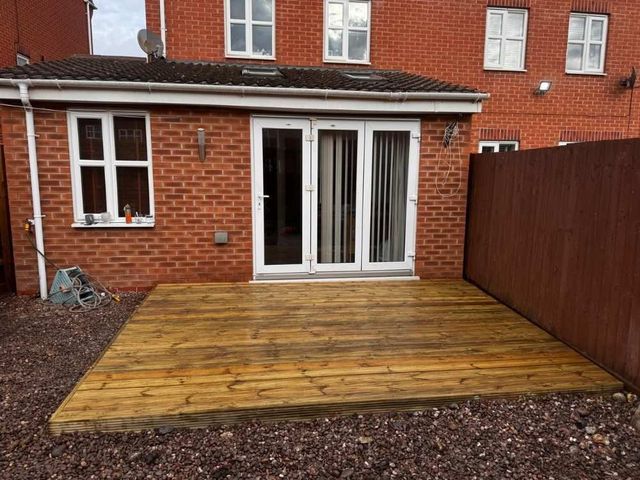 Small timber deck built outside bi-fold doors on a gravelled back garden behind a modern brick house