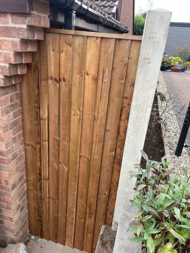 Featheredge wooden garden gate hung between a brick house corner and a concrete post, matching the adjoining fence