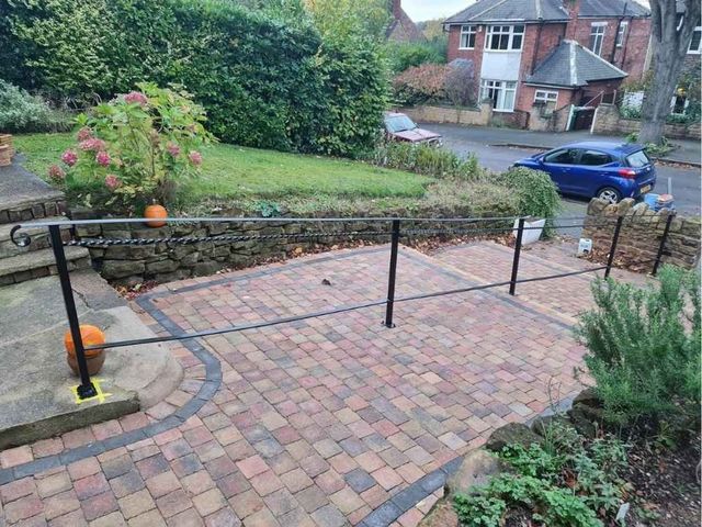 Black metal handrail running across a block paved front driveway with a twisted top rail